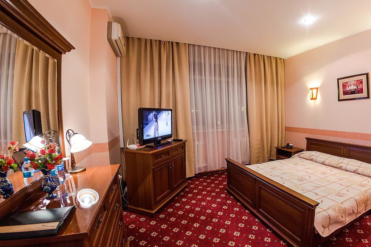 Een hotelkamer met een bed, een televisie, een bureau met een lamp en een spiegel.