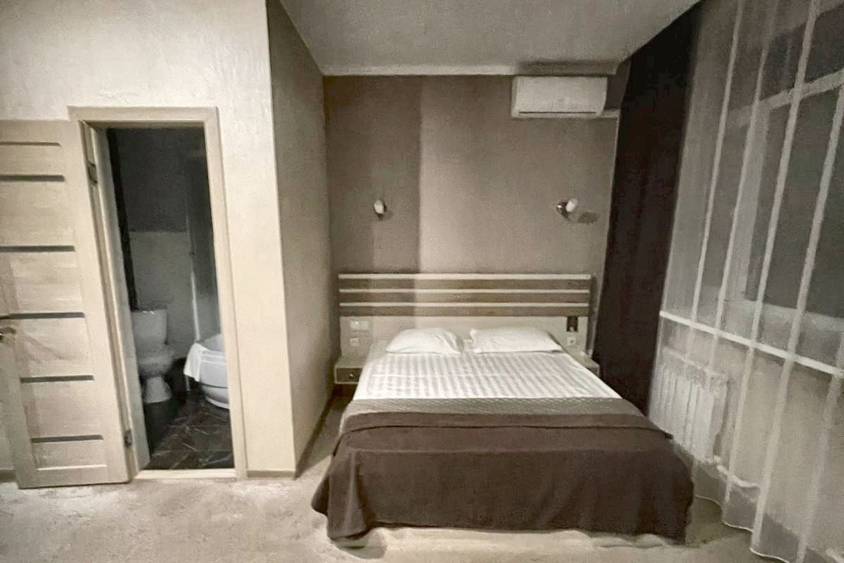 Een slaapkamer met een bed, een deur naar een badkamer en een raam met gordijnen.