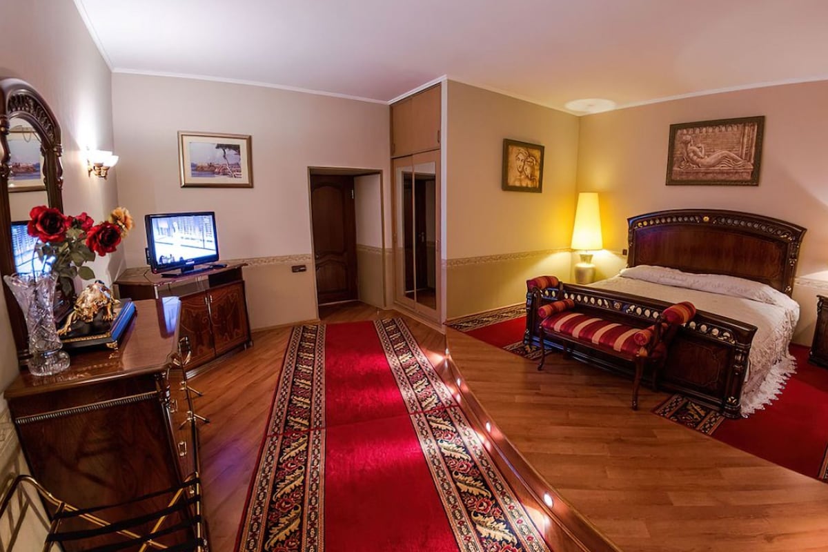Een hotelkamer met een bed, een bureau met een computer, een spiegel en een rood tapijt.