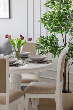 A dining table with plates and a vase of flowers, surrounded by chairs with cushions. - Bright Studio with Balcony in City Centre by Noclegi Renters (Warszawa)