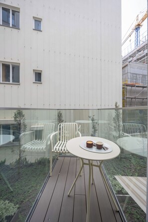 A glass-enclosed outdoor area with a round table and two chairs, a small table with a cup and a pastry, and a view of a building with windows and scaffolding. - Bright Studio with Balcony in City Centre by Noclegi Renters (Warszawa)