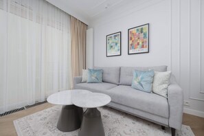 Ein modernes Wohnzimmer mit einem grauen Sofa, zwei gerahmten Kunstwerken, einem runden Couchtisch und einem gemusterten Teppich.