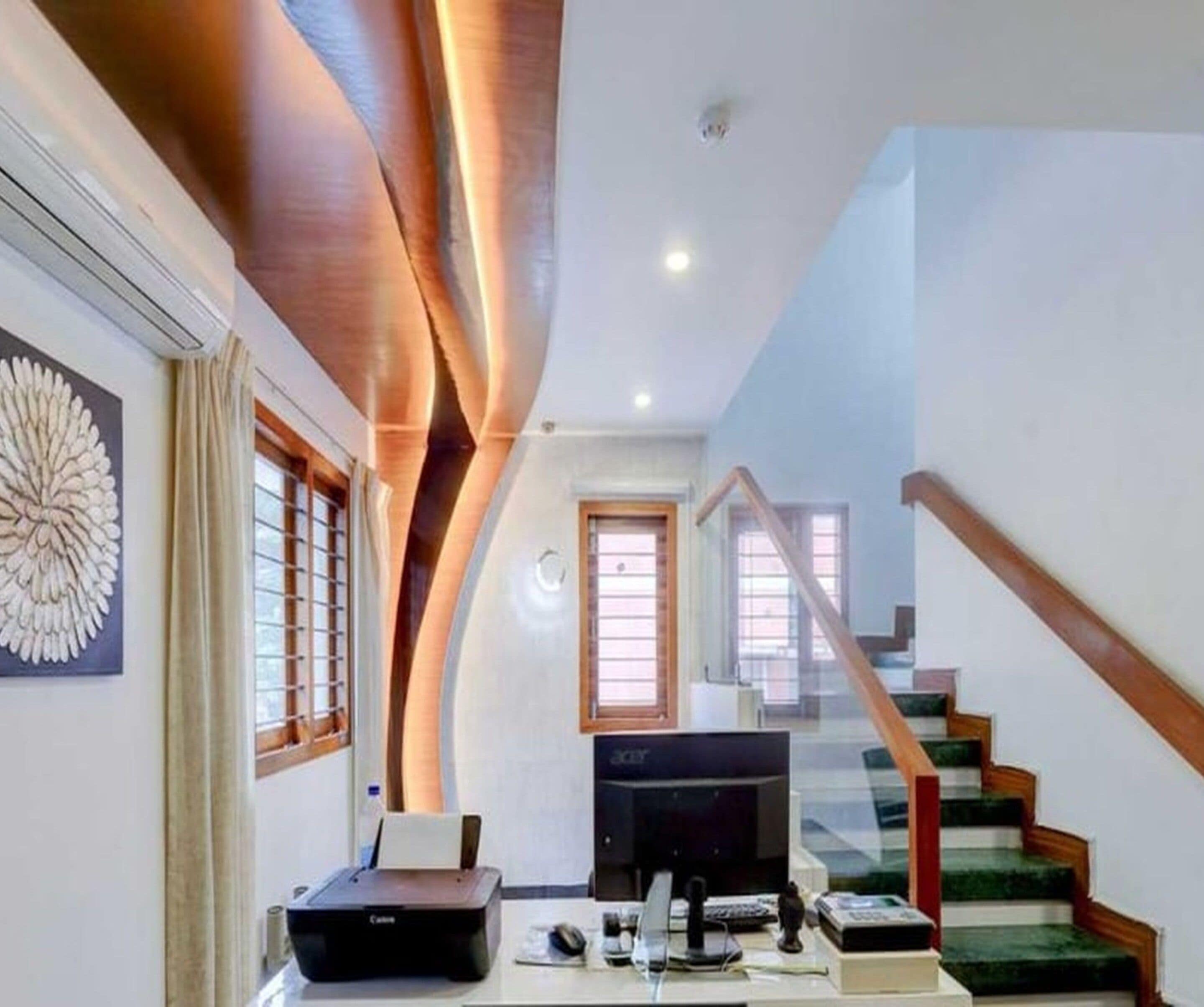 A modern living room with a flat-screen TV, a printer, and a staircase leading to an upper level.