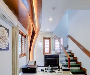 A modern living room with a flat-screen TV, a printer, and a staircase leading to an upper level.