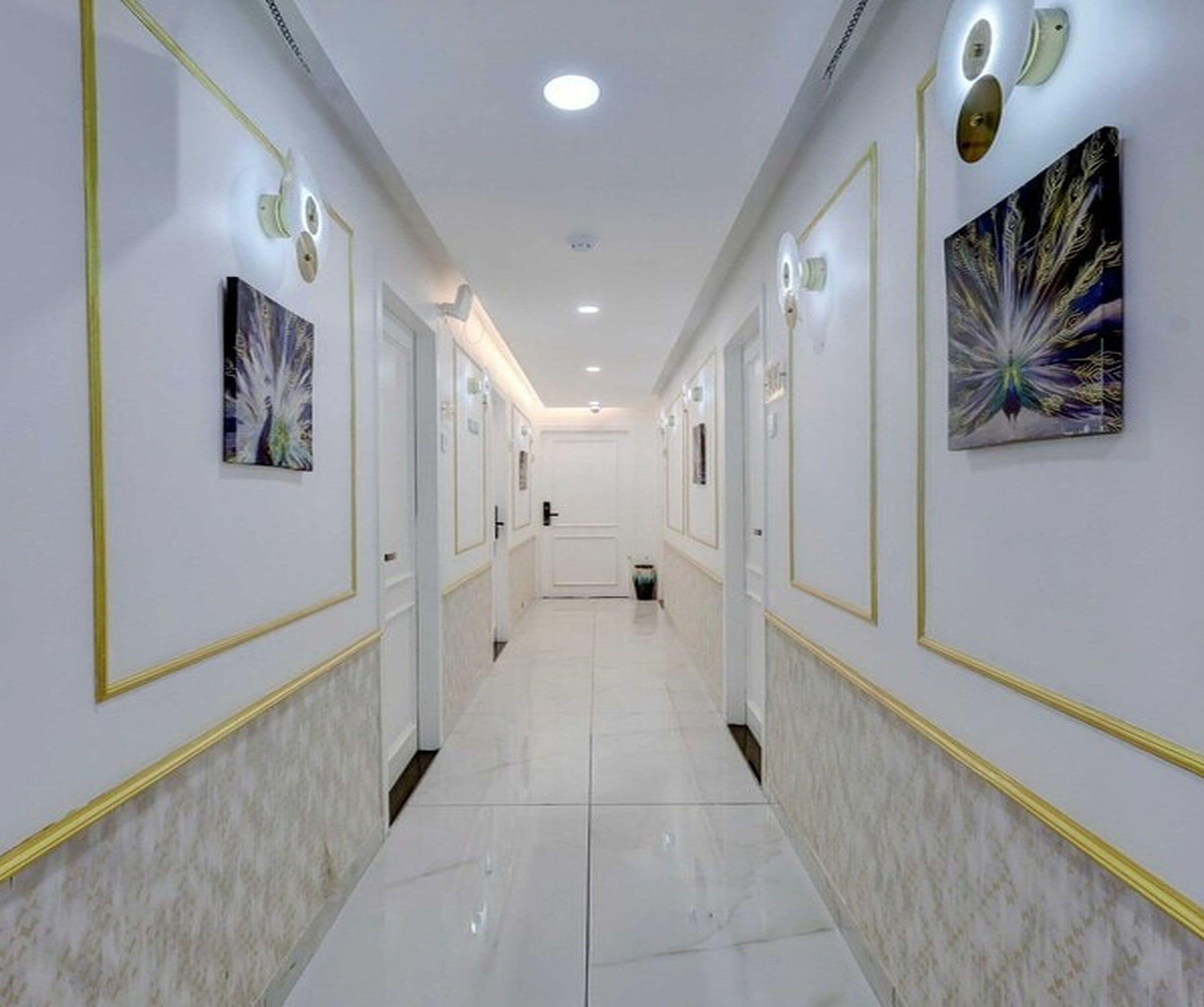 A hotel hallway with white walls, gold trim, and artwork.
