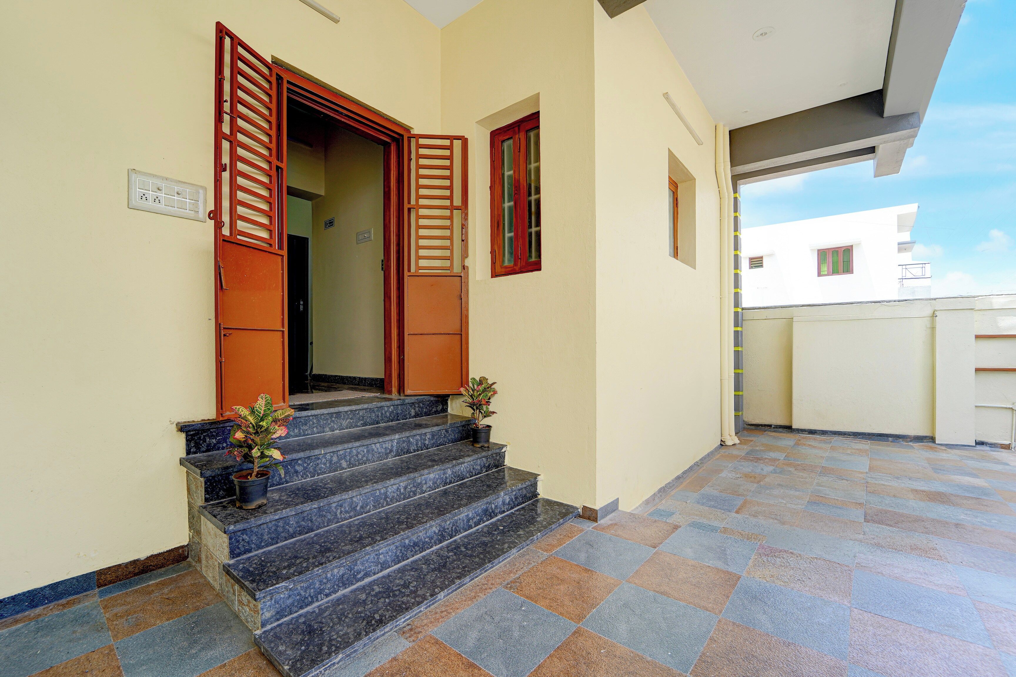Entrada de um edifício com um conjunto de degraus que levam a uma porta, uma pequena planta em vaso nos degraus e piso de azulejos.