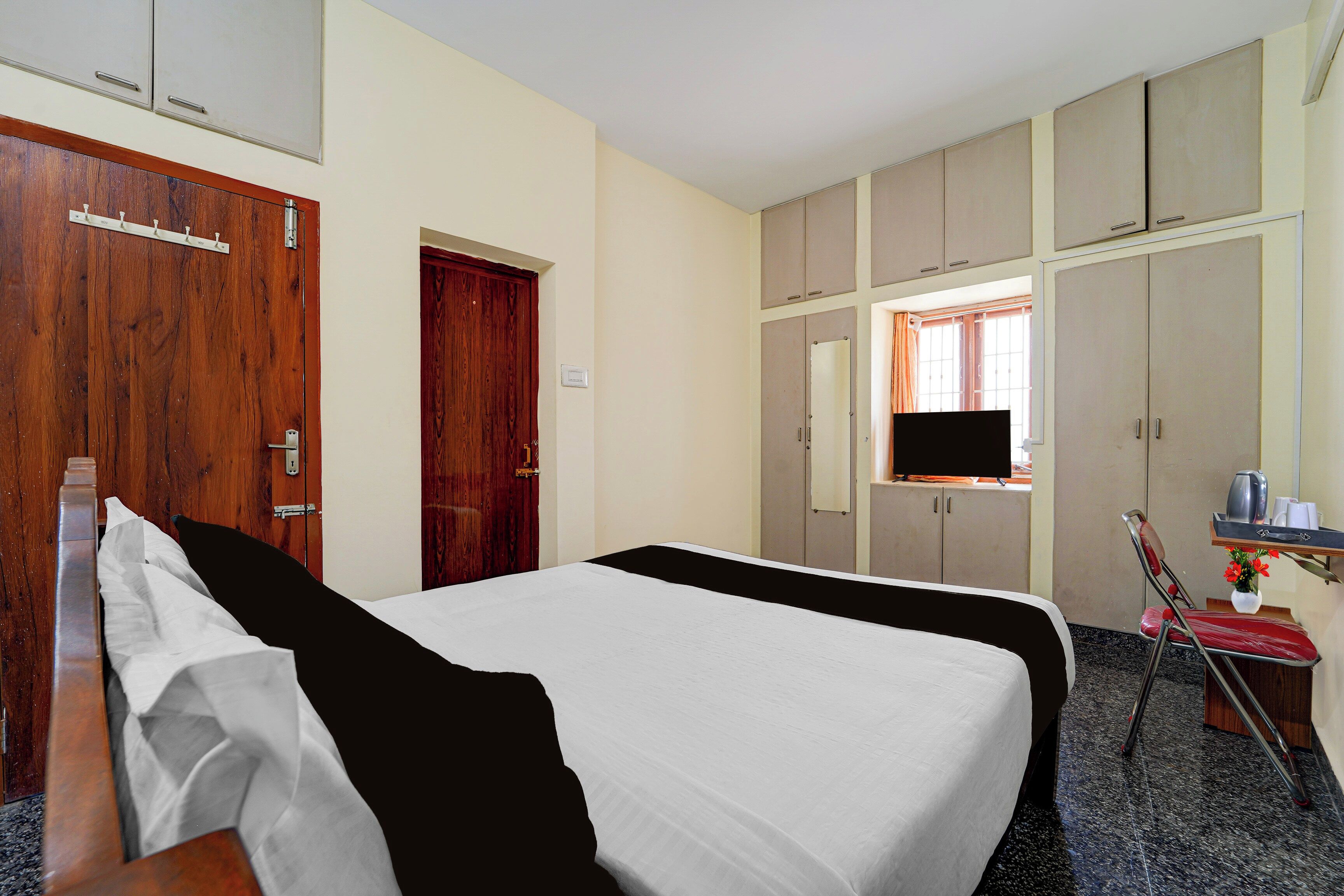 A hotel room with a bed, a desk with a chair, a wardrobe, and a window with curtains.