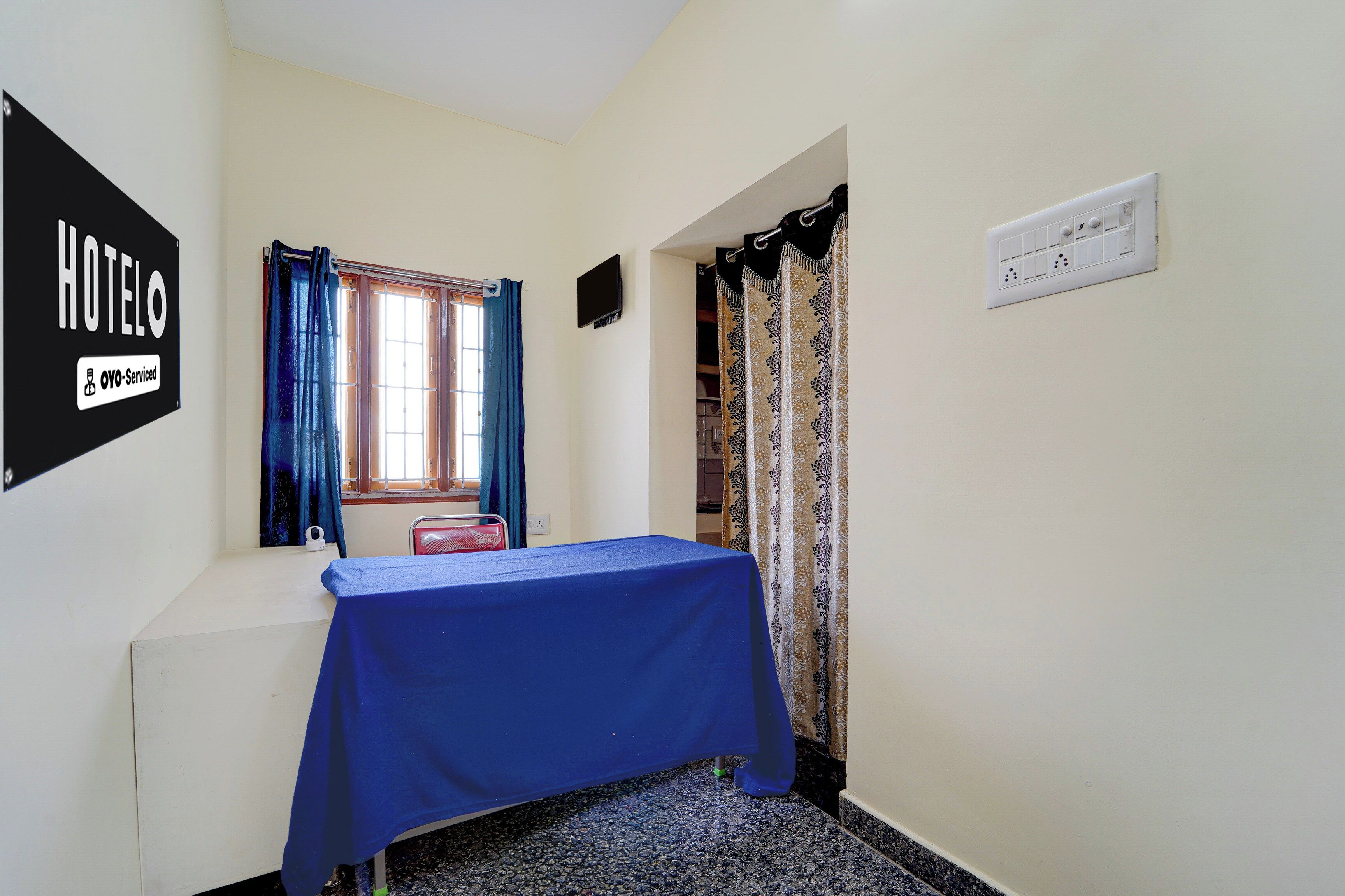A small room with a bed, a window with curtains, a wall-mounted TV, and a sign indicating the room is serviced by OYO.
