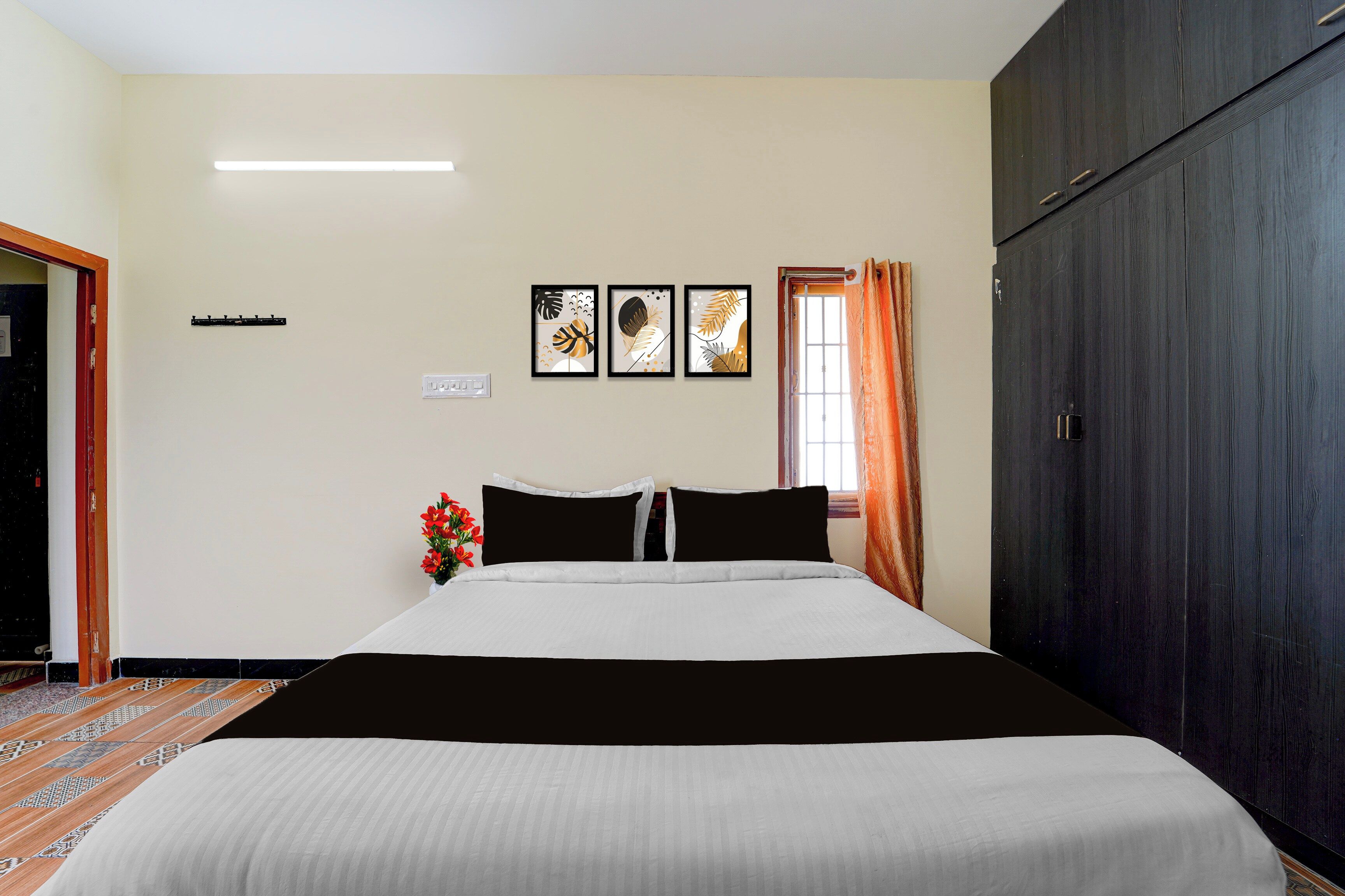 Quarto de hotel com cama, armário, janela com cortinas e três obras de arte emolduradas na parede.