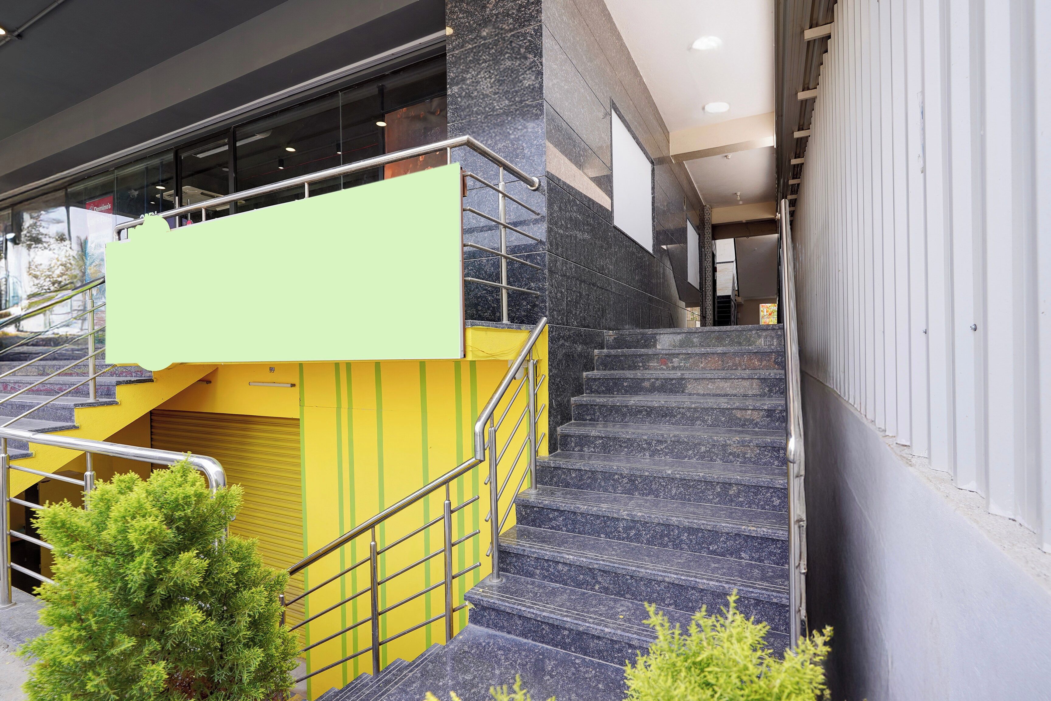 Una scala con ringhiera gialla e piattaforma verde, che conduce all'ingresso di un edificio.