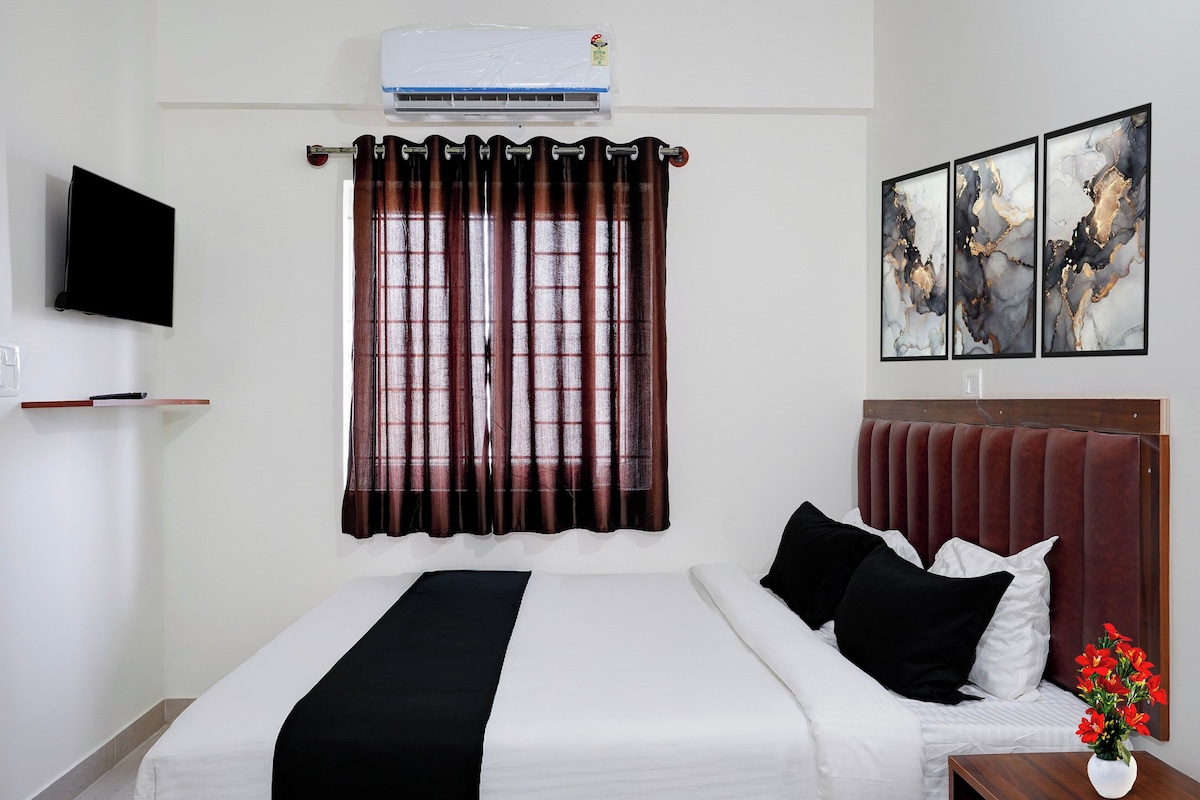 A hotel room with a bed, a flat-screen TV, a window with curtains, and artwork on the wall.