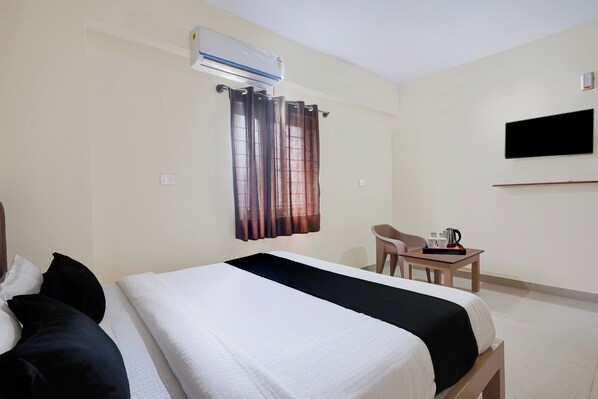 Habitación de hotel con cama, escritorio con cafetera, televisión y aire acondicionado.