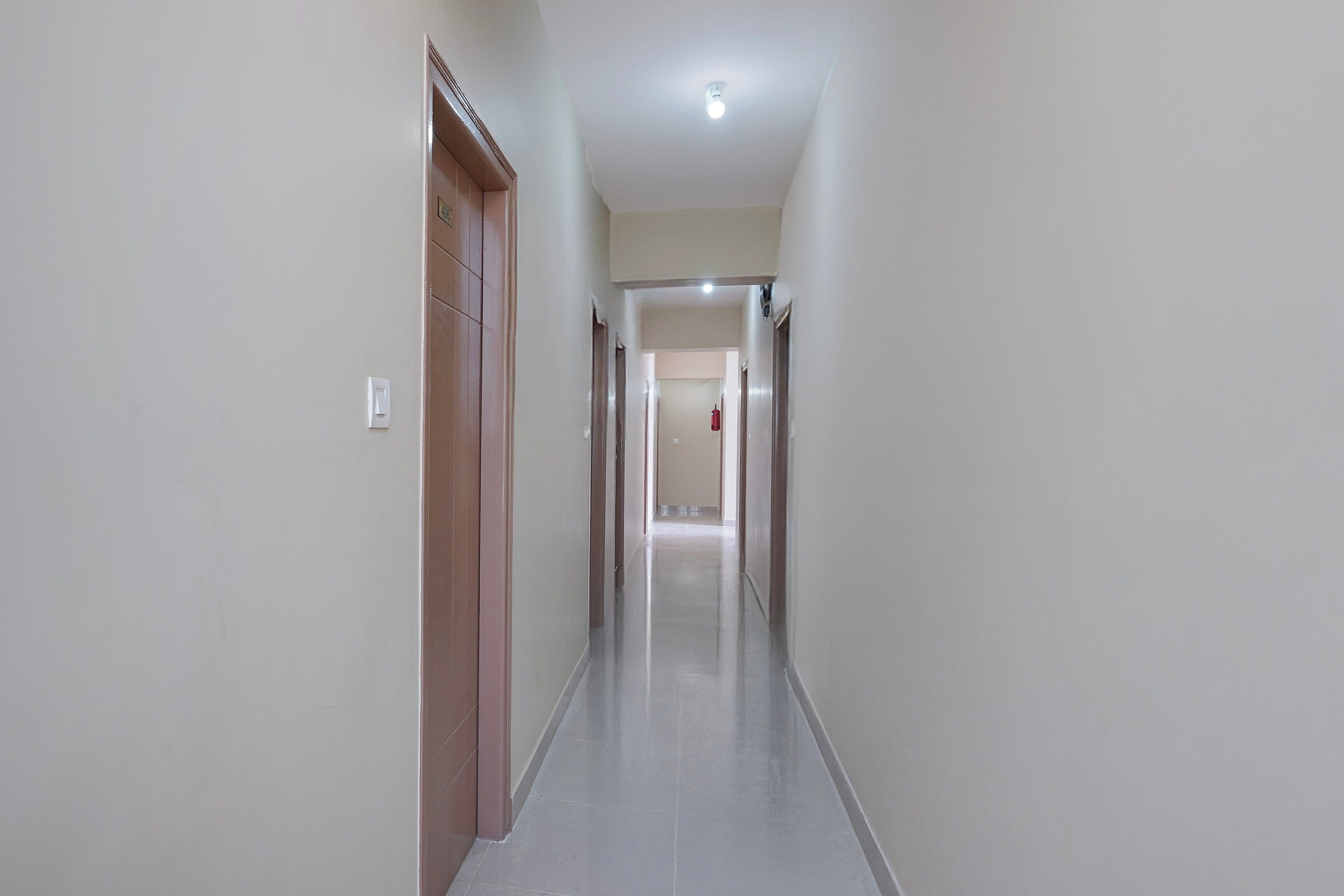 Un pasillo estrecho y bien iluminado con piso de baldosas, que conduce a una puerta al final.