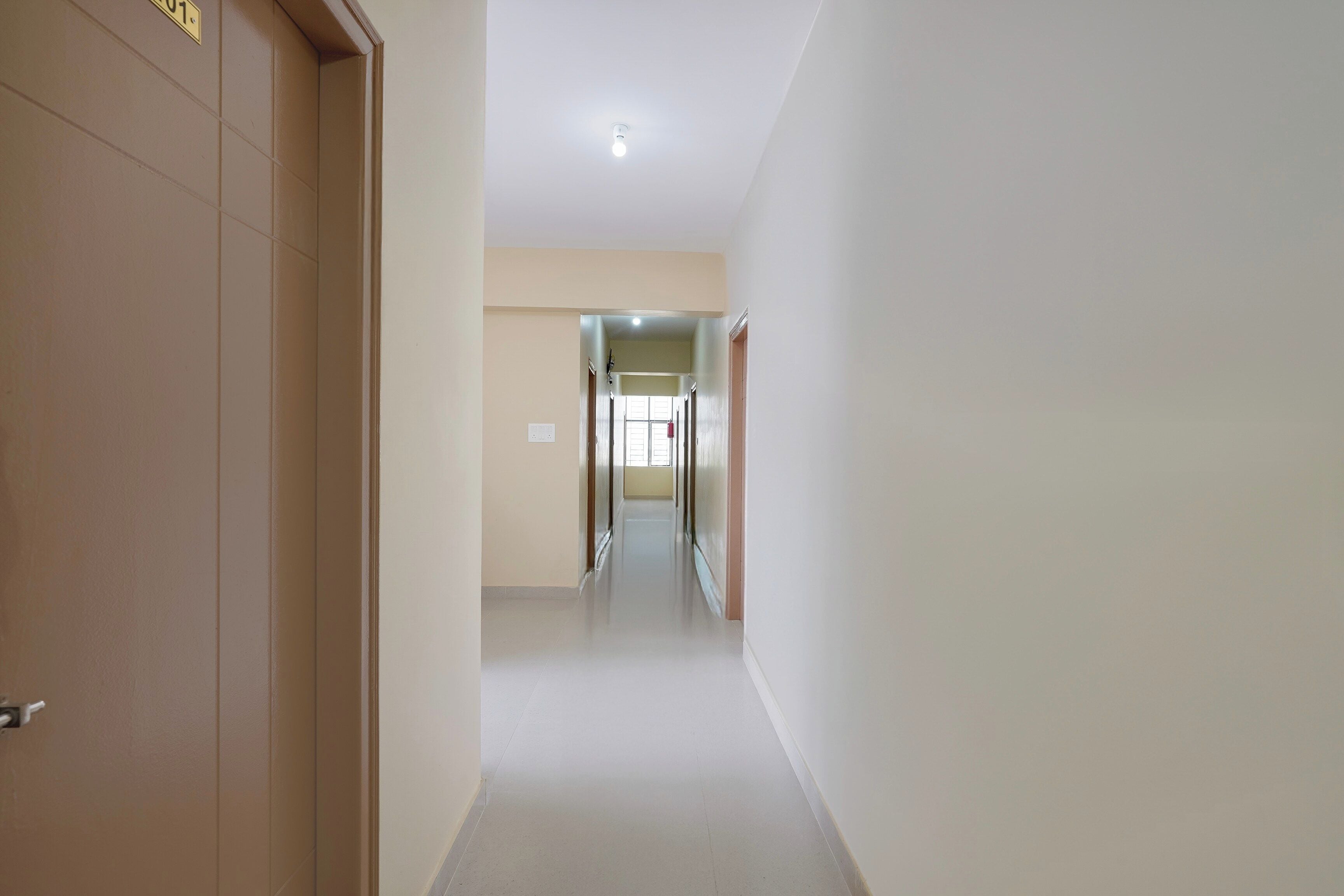 Un couloir avec une porte à gauche et une fenêtre au fond.