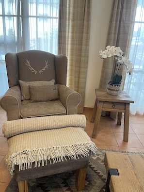 A brown armchair with a cushion, a woven throw, and a decorative plant on a wooden side table. - New Listing (Laax)