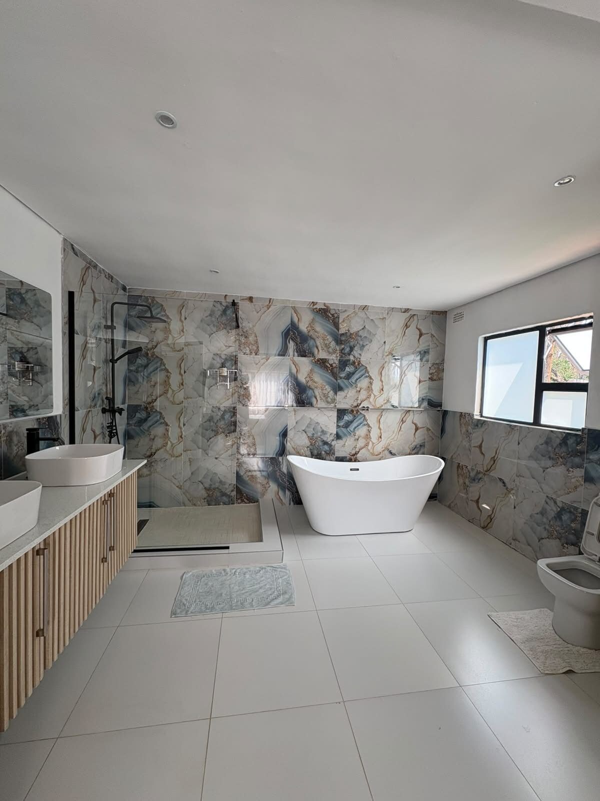 A modern bathroom with a freestanding bathtub, two sinks, and a glass shower enclosure.