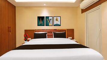 A hotel room with a bed, a nightstand, a vase with flowers, and three framed artworks on the wall.