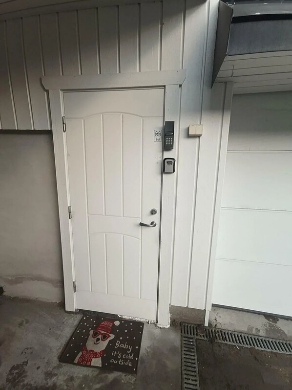 A white door with a keypad lock, a doormat with a baby-themed design, and a garage door.