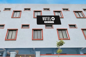 A hotel facade with multiple windows, a central sign reading 'HOTELO' and 'OYO-Serviced', and a small tree in the foreground.