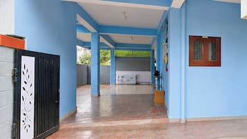 A covered outdoor area with blue walls and a tiled floor, leading to a building entrance.