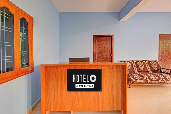 A hotel reception desk with a sign indicating it is oyo-serviced. There is a bed with a patterned cover in the background.
