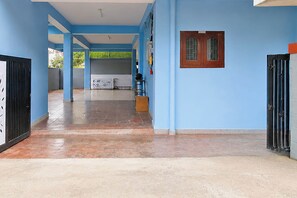 Un passadís amb parets blaves i un terra emplastrat, que condueix a una habitació amb una finestra i una porta.