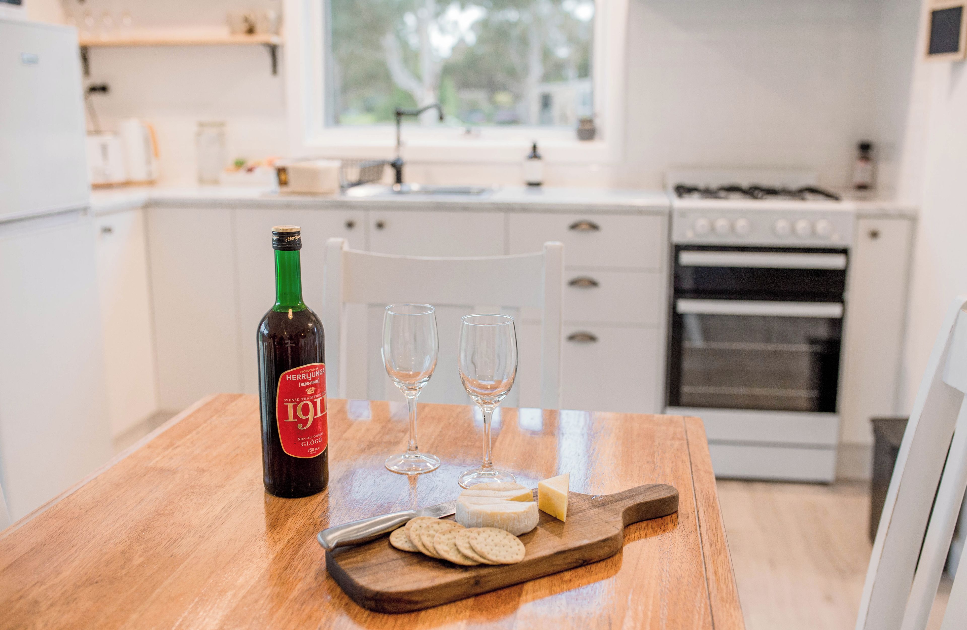 A kitchen with a wooden table, a bottle of wine, two glasses, and a cheese board with crackers.