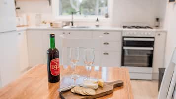 Uma cozinha com mesa de madeira, uma garrafa de vinho, dois copos e uma tábua de queijos com biscoitos.
