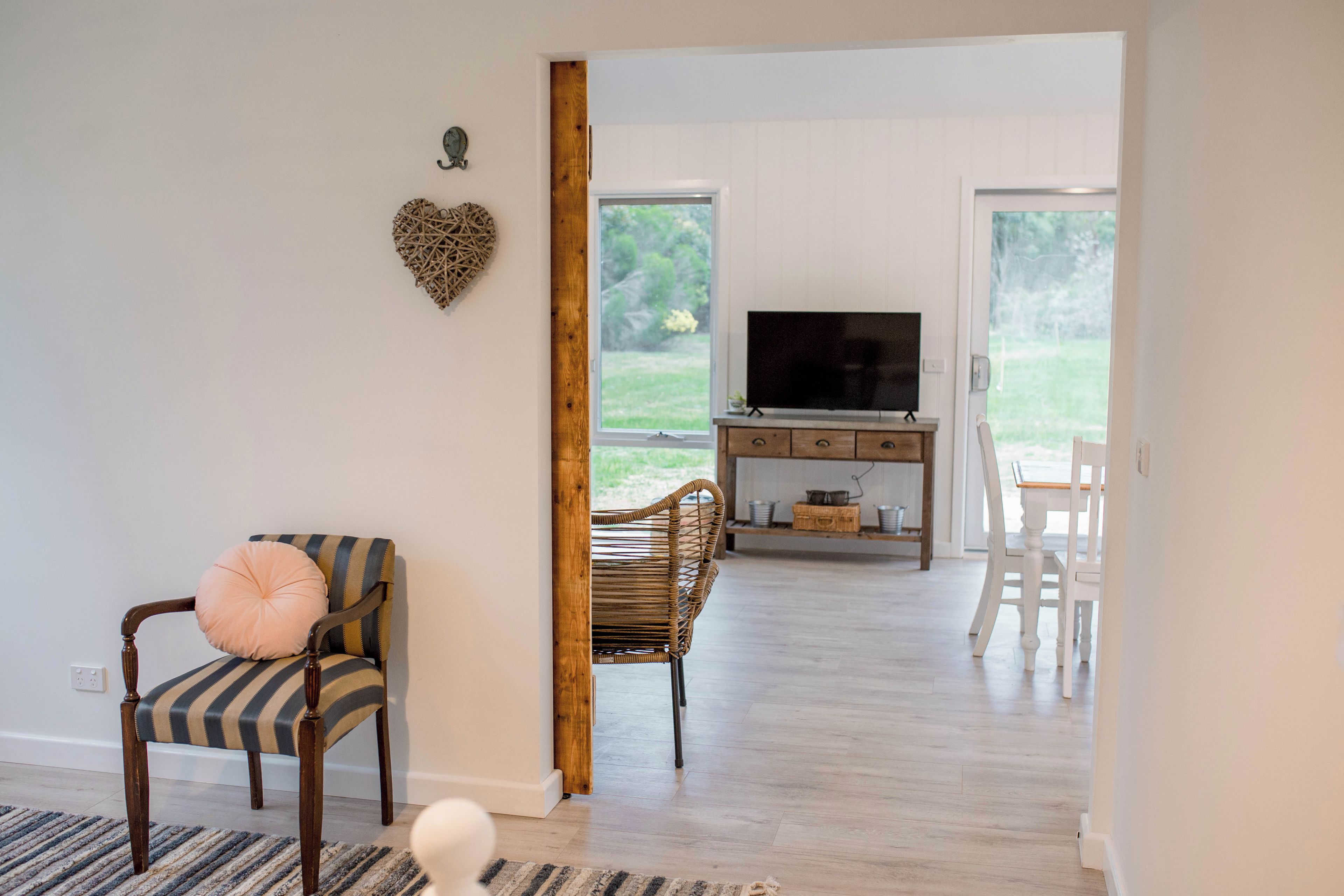 Uma sala de estar com televisão, sofá, poltrona e uma decoração em formato de coração na parede.