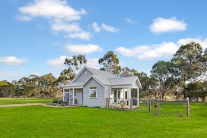 A single-story house with a covered porch, surrounded by a fenced yard and trees.