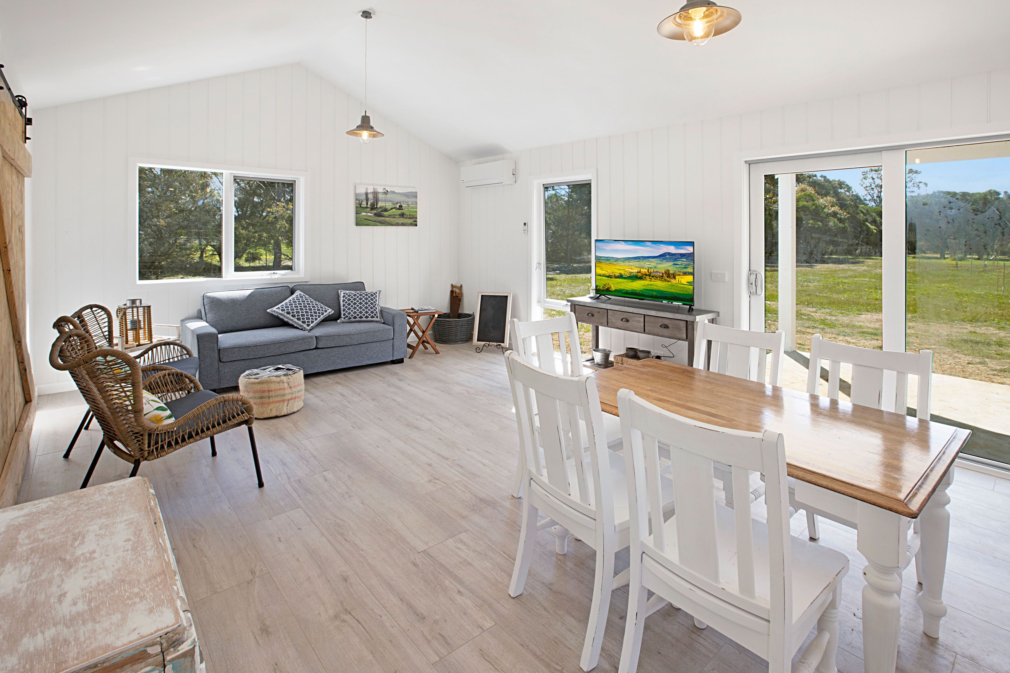 A spacious living area with a sofa, dining table, and chairs, large windows with a view of the outdoors.