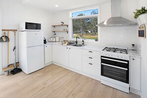 Une cuisine moderne avec des meubles blancs, un four encastré, une cuisinière à gaz et une fenêtre donnant sur un jardin.