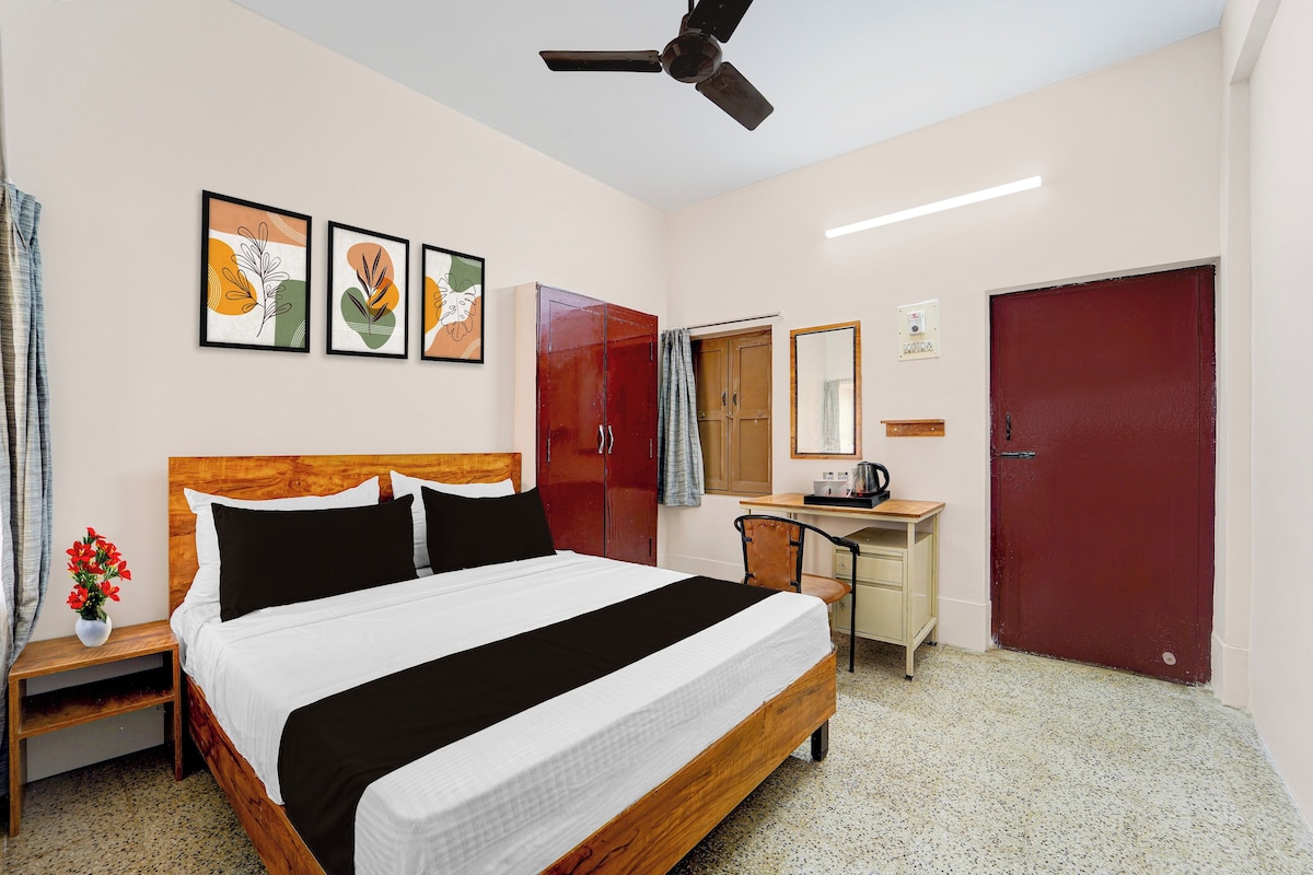 Habitación de hotel con cama, escritorio, armario, ventilador de techo y obras de arte en la pared.