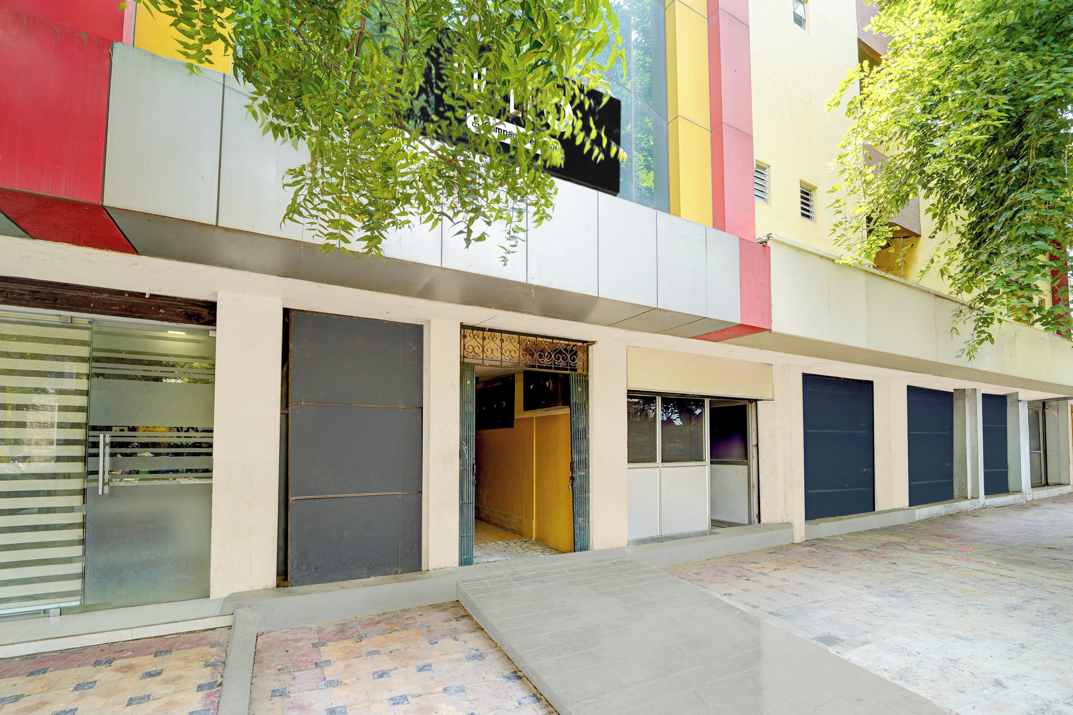 A building with multiple garage doors, a tiled entrance area, and a tree with green leaves.