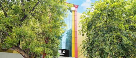 A building with a prominent vertical structure, a sign reading 'TELO', and lush green trees surrounding the area.