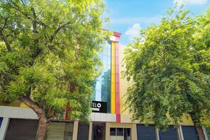 Un edificio con una estructura vertical destacada, un letrero que dice 'TELO' y exuberantes árboles verdes que lo rodean.