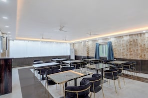 Un salón de conferencias con mesas y sillas, ventiladores de techo y papel tapiz estampado.