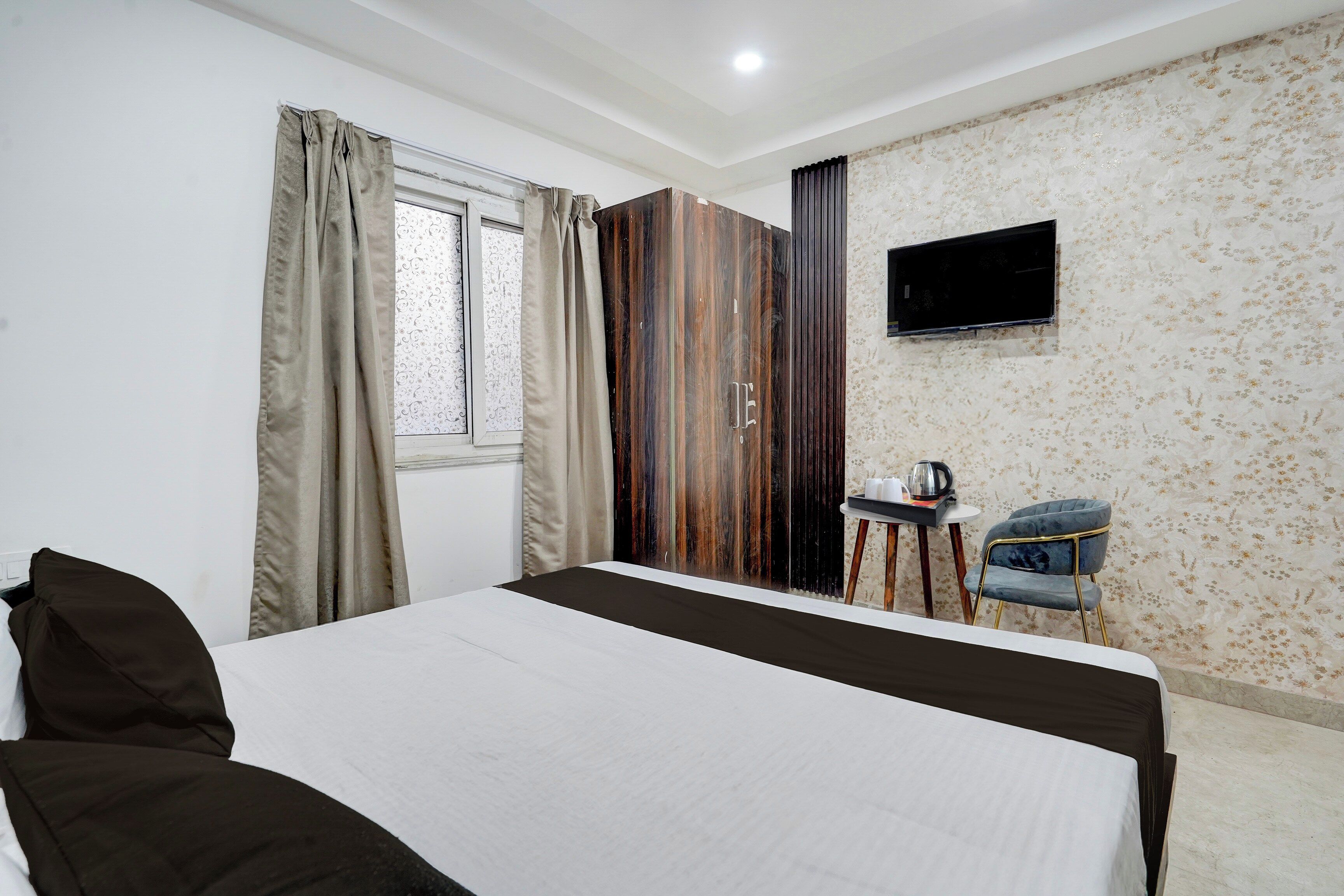 Ein Hotelzimmer mit Bett, Schreibtisch mit Stuhl, Fernseher und einem Fenster mit Vorhängen.