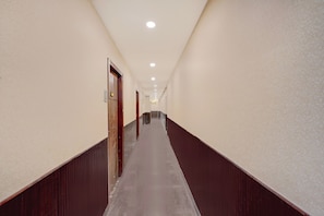Un largo y estrecho pasillo de hotel con piso de madera y paredes, que conduce a una puerta al final.