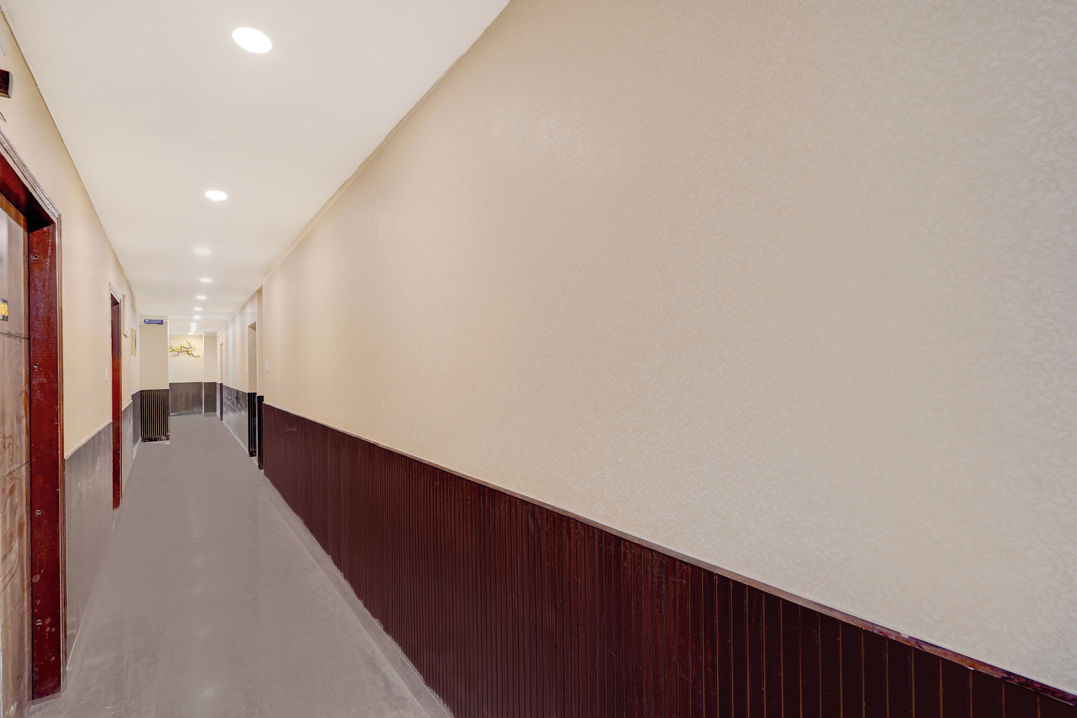 A long, narrow hallway with a wooden baseboard, white walls, and a series of recessed ceiling lights.