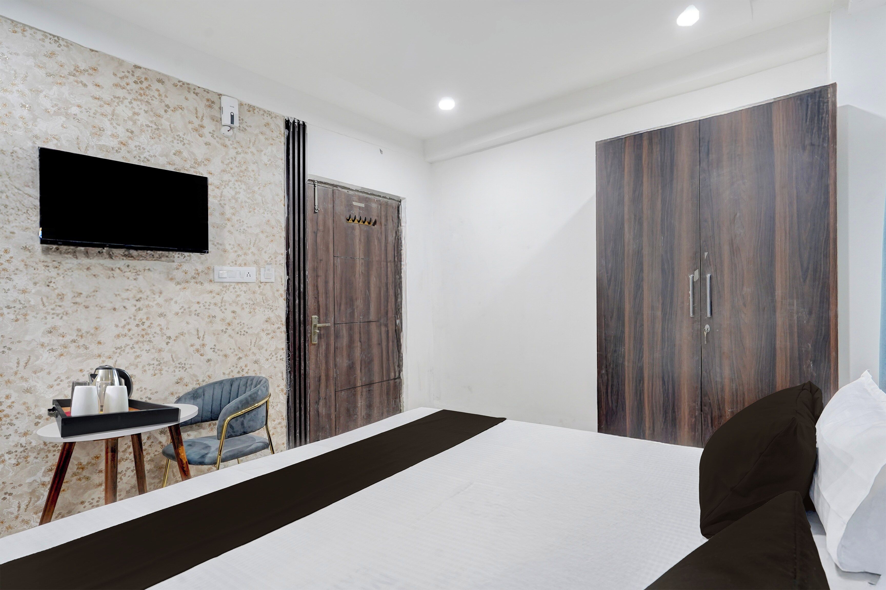 A hotel room with a bed, a TV mounted on the wall, a desk with a chair, and two wardrobes.