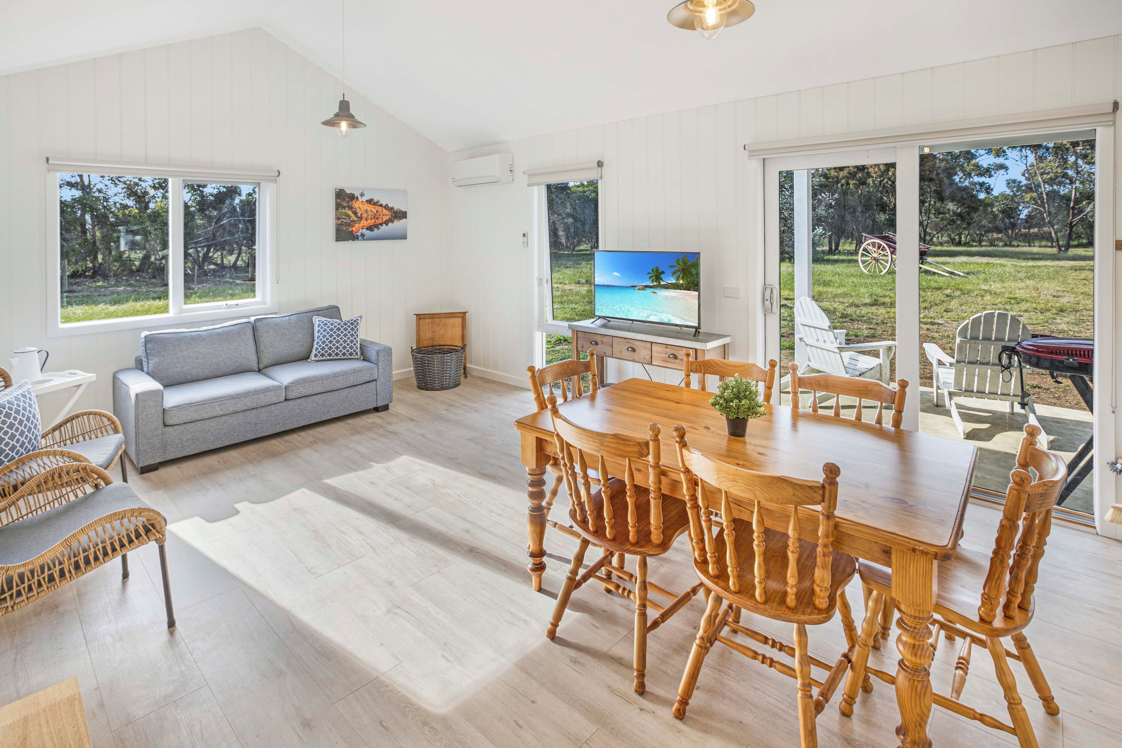 A spacious living area with a sofa, dining table, and chairs, a television, and large windows offering views of the outdoors.