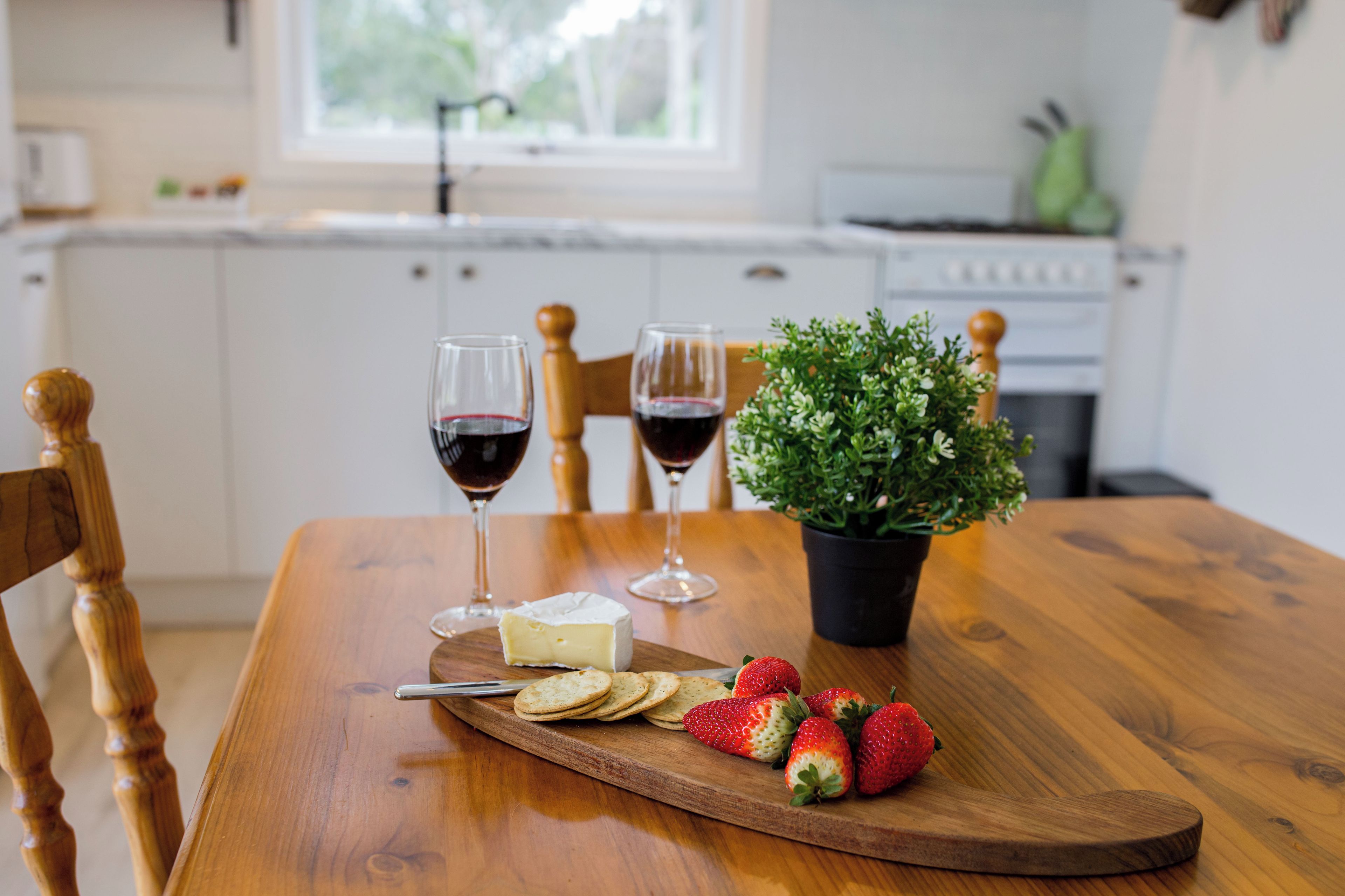 Een houten tafel met kaas, aardbeien, crackers en twee glazen rode wijn.