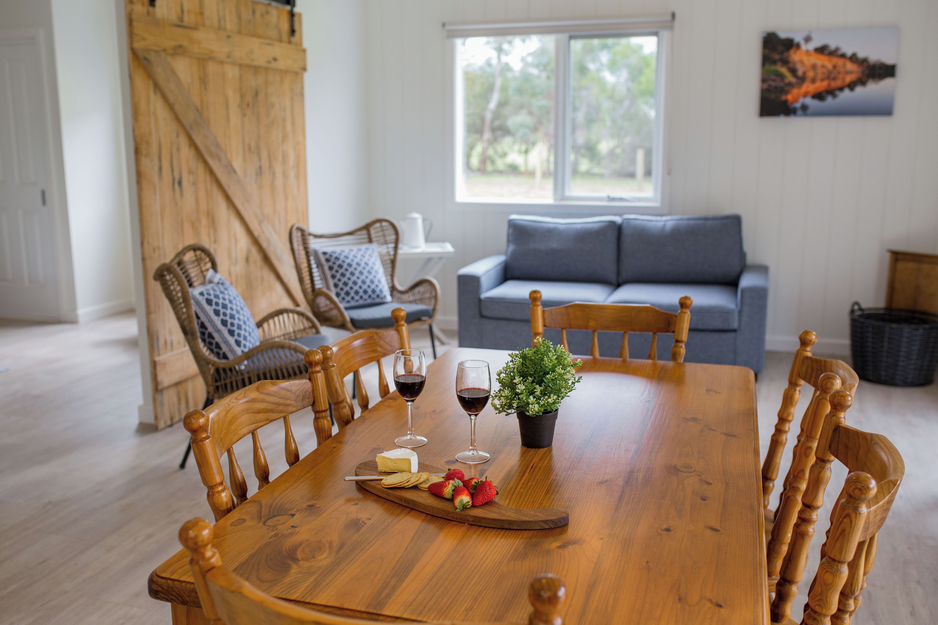 A dining table with chairs, a wooden bench, a potted plant, a cheese platter, and glasses of red wine.
