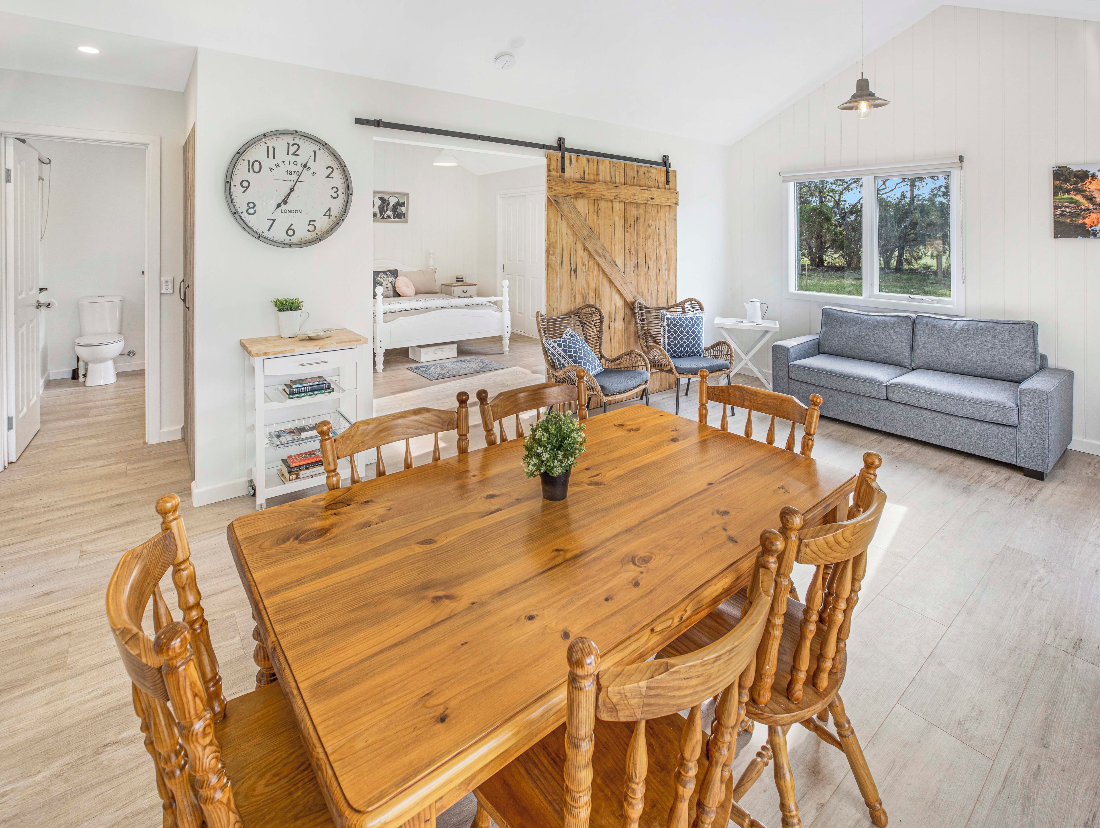 Une pièce spacieuse avec une table à manger en bois, des chaises, un canapé et une grande horloge au mur.