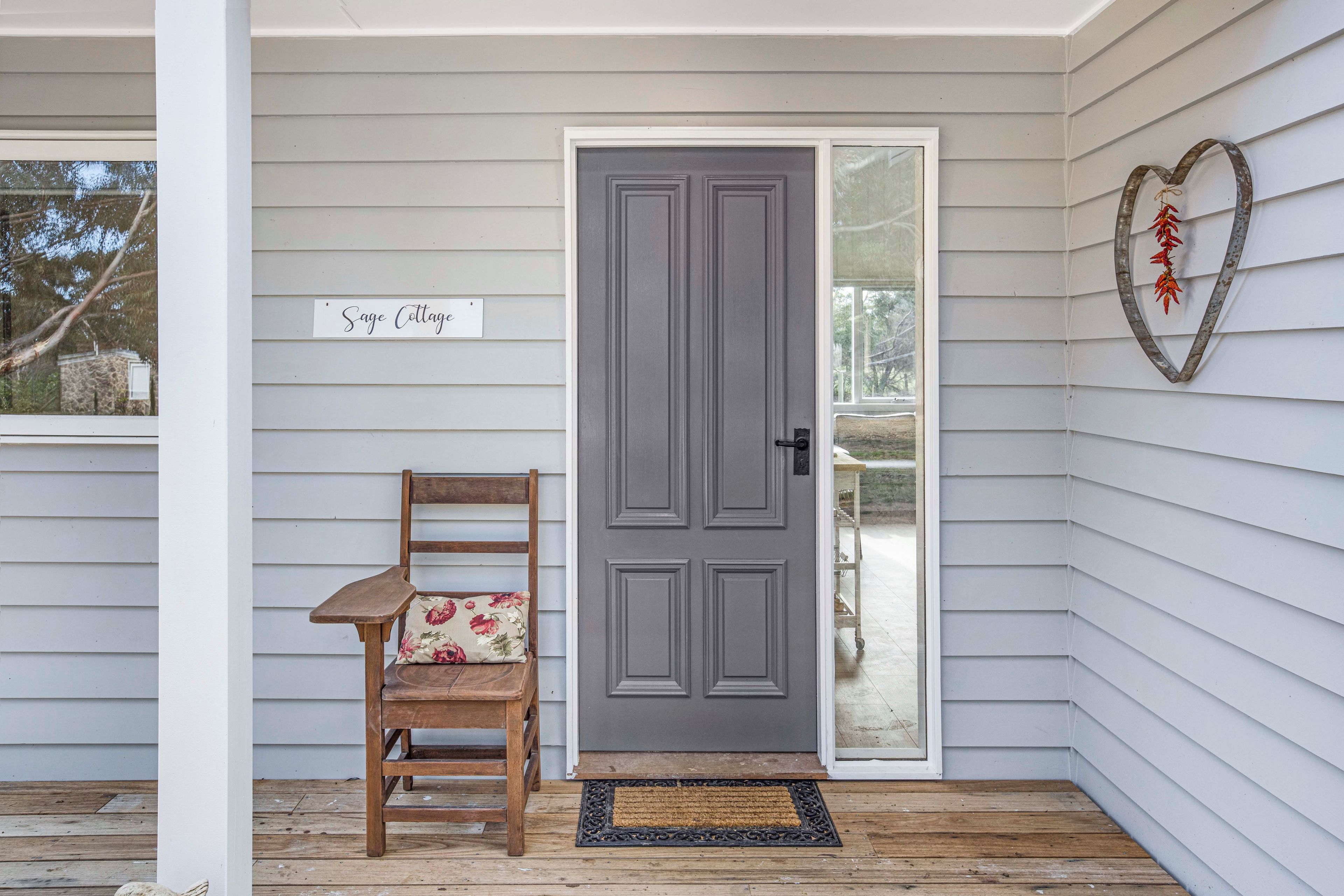 A porch with a wooden chair, a grey door, and a sign that reads 'Sage Cottage'.