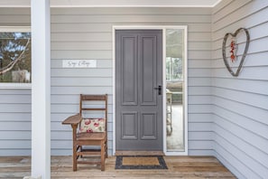 A porch with a wooden chair, a grey door, and a sign that reads 'Sage Cottage'.