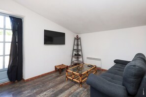 En stue med en sofa, fjernsyn monteret på væggen, et lille træbord og en reolstiger.