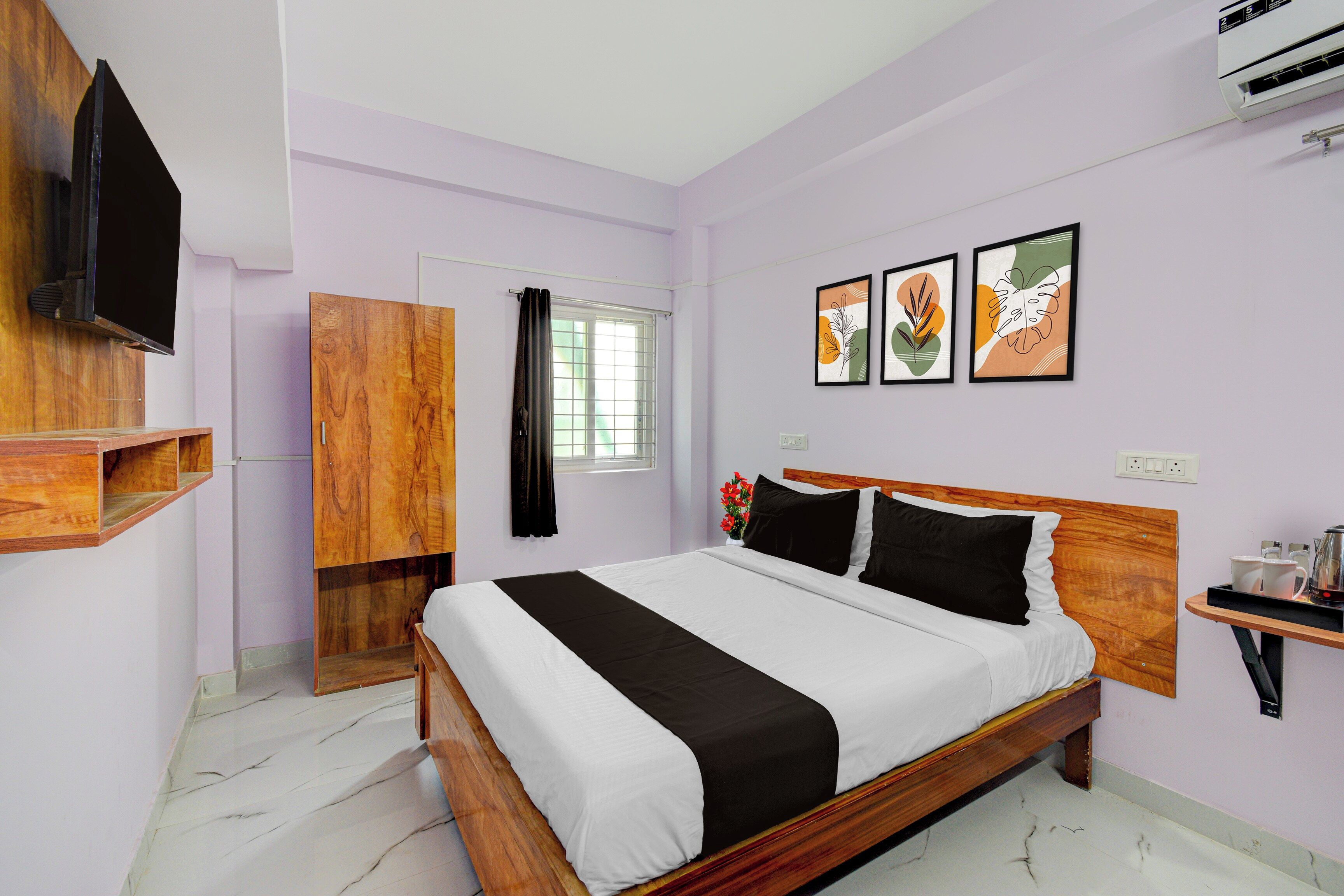 A bedroom with a bed, a TV, a wardrobe, a window with curtains, and artwork on the wall.