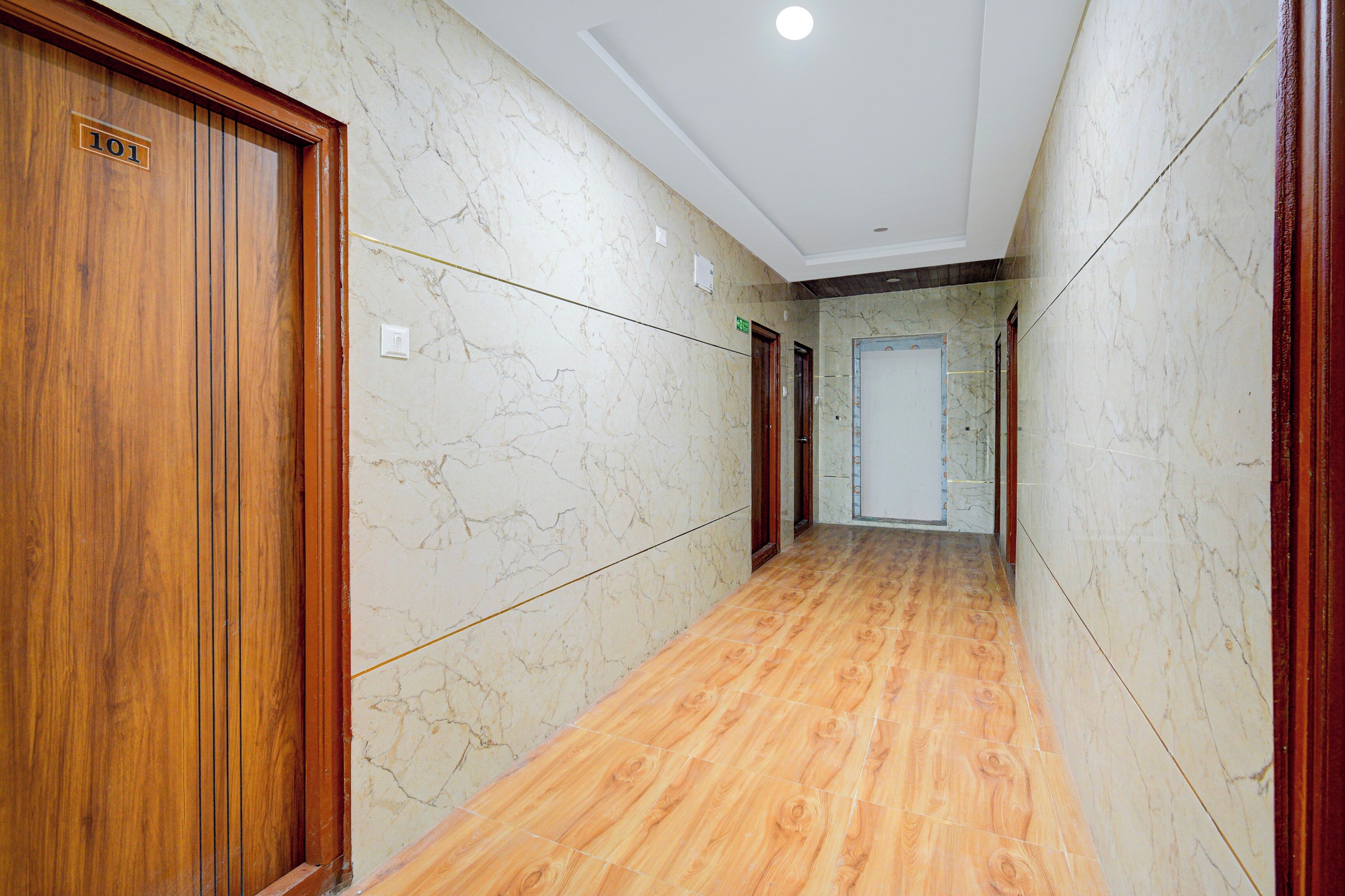 A hallway with marble walls and wooden flooring, leading to a door with a sign indicating an elevator.